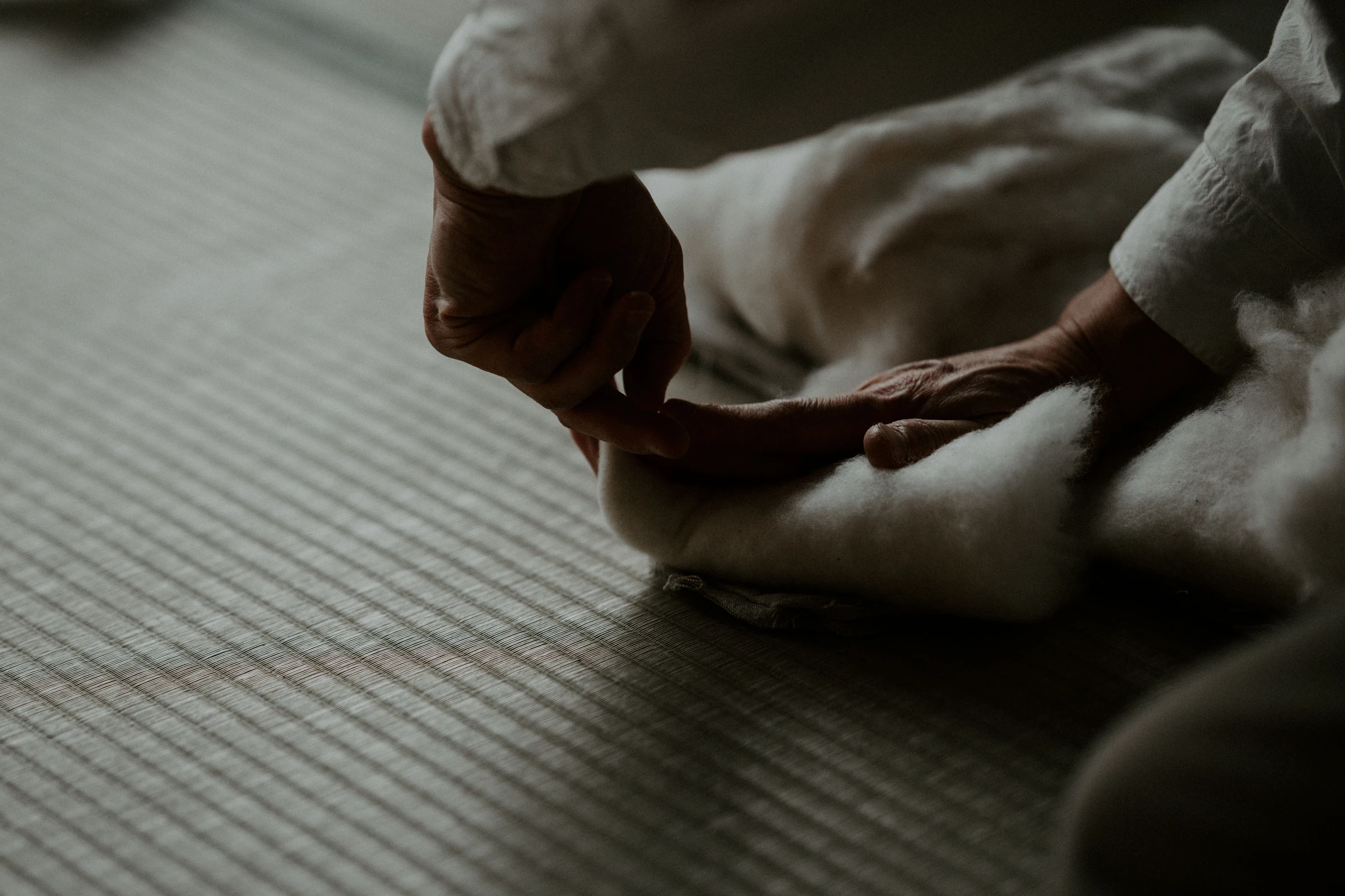 Hands spreading a sheet of cotton across tatami.