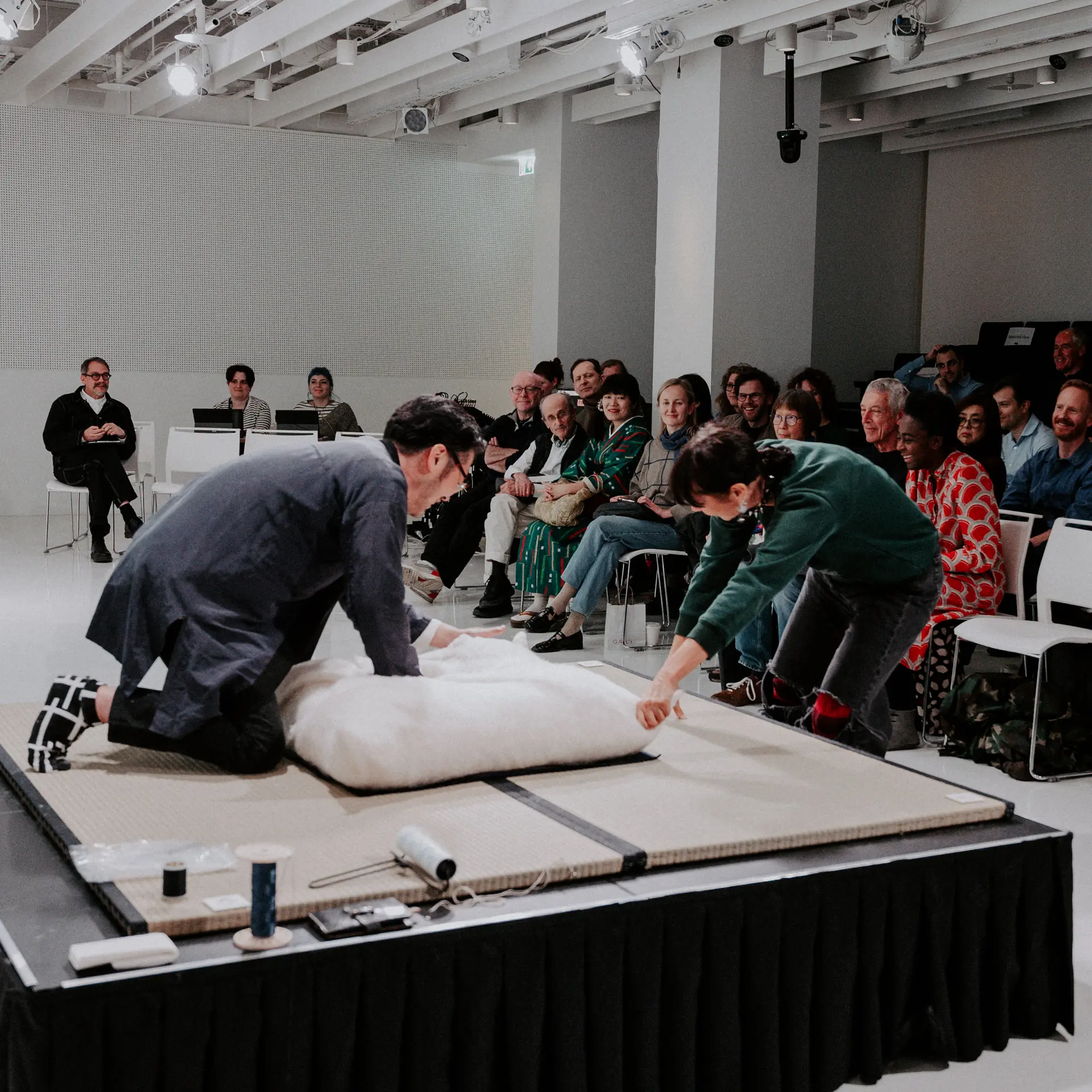 Takuya Niwa working cotton on a low platform in front of an audience.